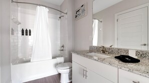A modern bathroom with a glass-enclosed shower, a white toilet, a granite countertop, and a large mirror.