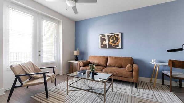 A living room with a brown sofa, a glass coffee table, a chair, and a lamp on a side table.