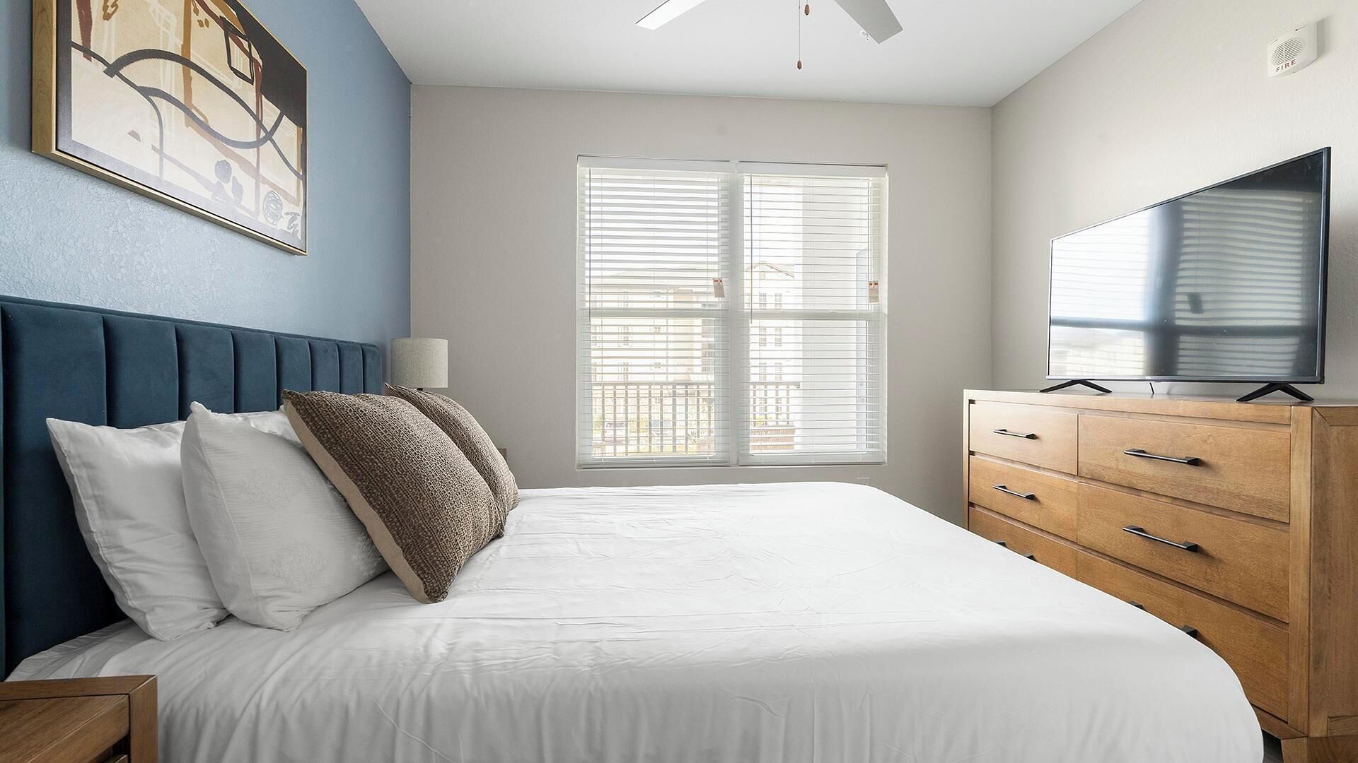 A bedroom with a bed, a TV, a dresser, and a window with blinds.