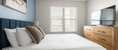 A bedroom with a bed, a TV, a dresser, and a window with blinds.