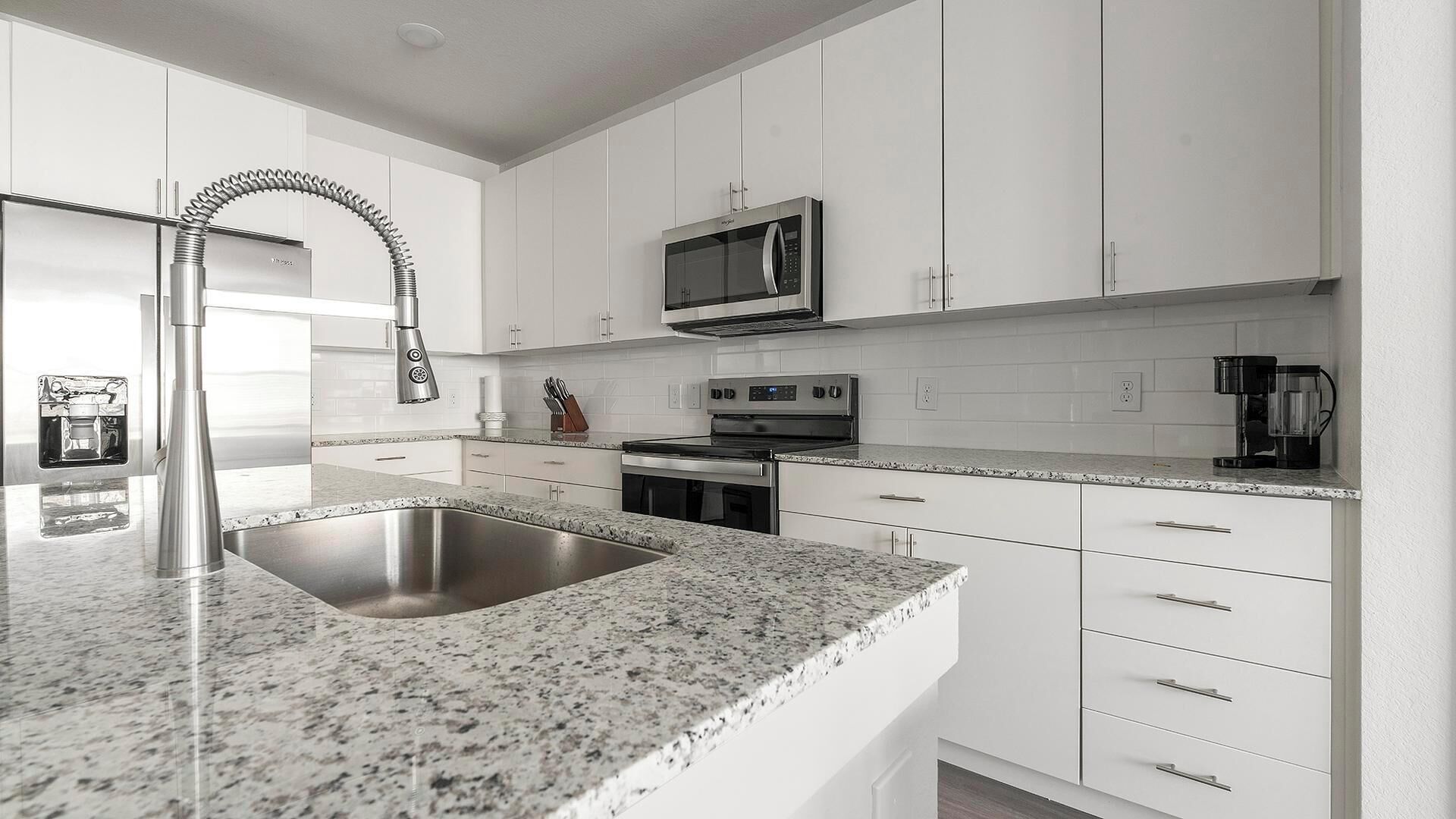 A modern kitchen with white cabinets, a stainless steel sink, a built-in microwave, and a coffee maker.