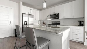 A modern kitchen with white cabinetry, a central island with seating, stainless steel appliances, and a pendant light. - Landing | Beautiful 2BD, Gym (Fort Myers)