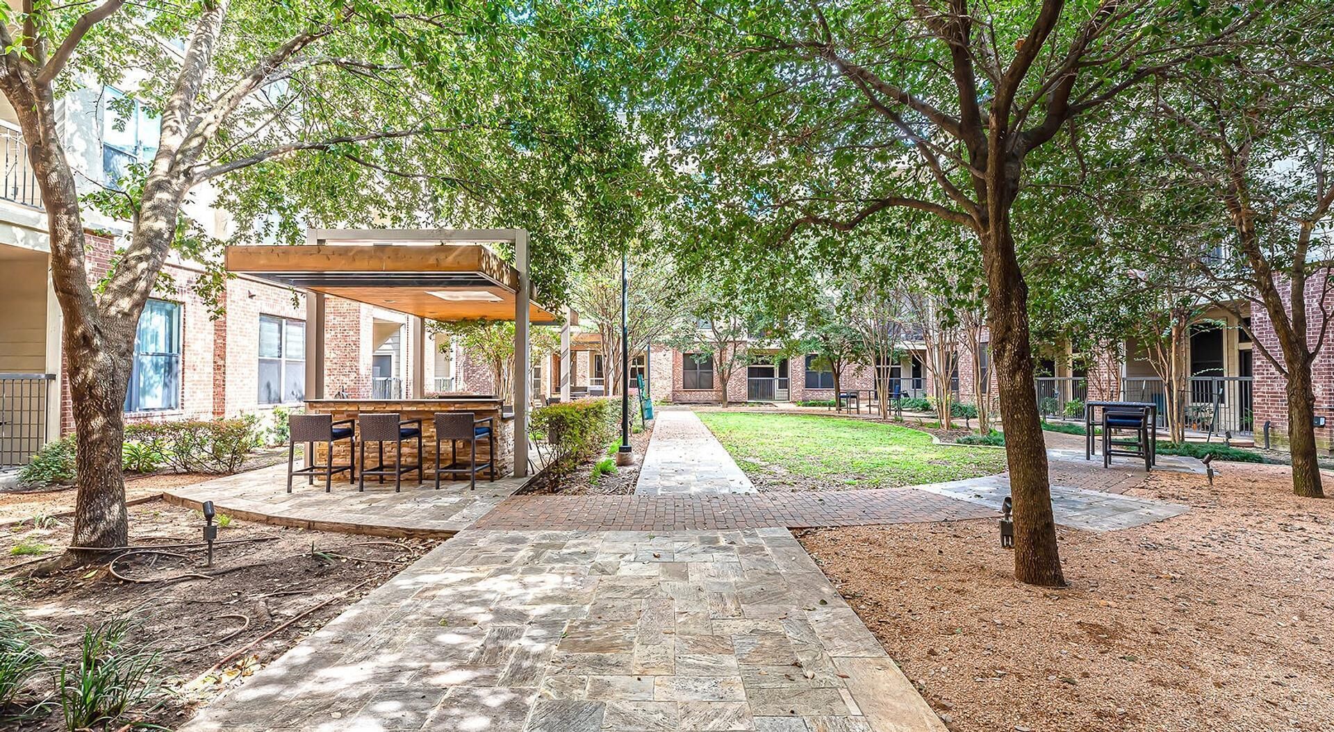 An outdoor patio area with a covered seating area and a pathway leading to a building.