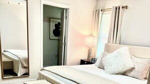 Ein Schlafzimmer mit einem großen Bett, einer Bank, einem Nachttisch, einem Spiegel und einer Tür.