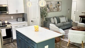 Eine moderne Küche mit einer zentralen Kochinsel, weißen Schränken und einem grauen Sofa im Wohnbereich.