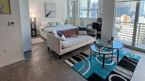 Una sala de estar moderna con un sofá, una mesa de centro de vidrio y vistas de la ciudad a través de amplios ventanales.