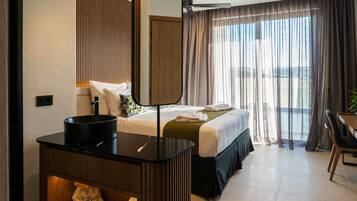 Habitación de hotel con cama, escritorio con espejo, secador de pelo y vistas al exterior a través de amplias ventanas.