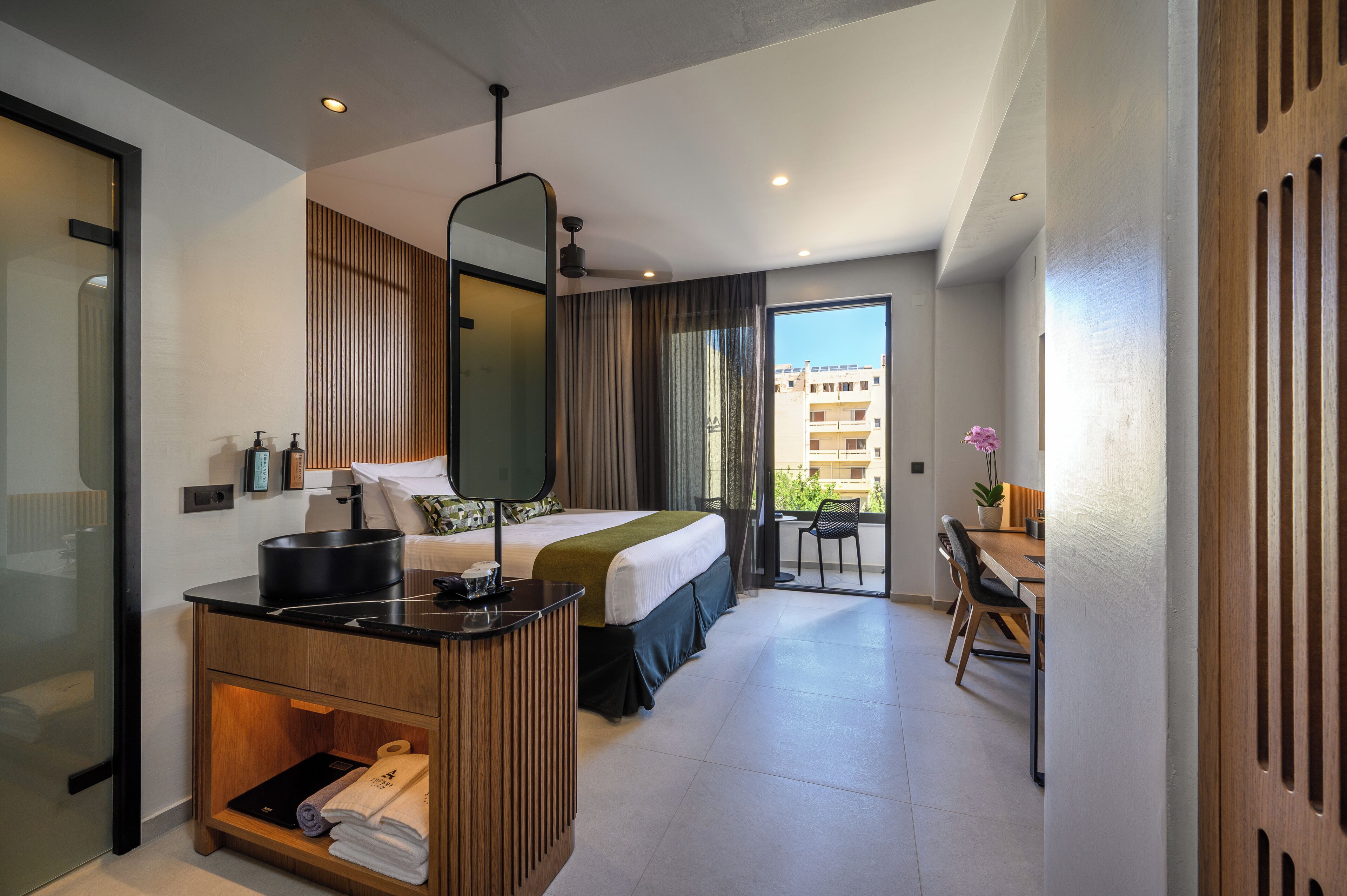 A modern hotel room with a bed, desk, and balcony.