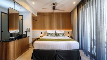 A modern bedroom with a large bed, a wooden desk, a ceiling fan, and a view of the outdoors through sheer curtains.