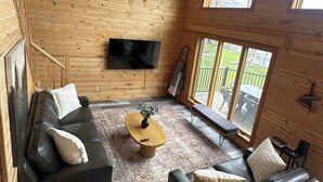 A wooden interior with a sofa, a coffee table, and a TV mounted on the wall. - Lakefront Escape with Loft & Summer Bunkhouse — Steps from the Water & Trails! (Waubun)