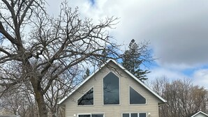 A two-story house with a deck, a dock, and a pond. - Lakefront Escape with Loft & Summer Bunkhouse — Steps from the Water & Trails! (Waubun)