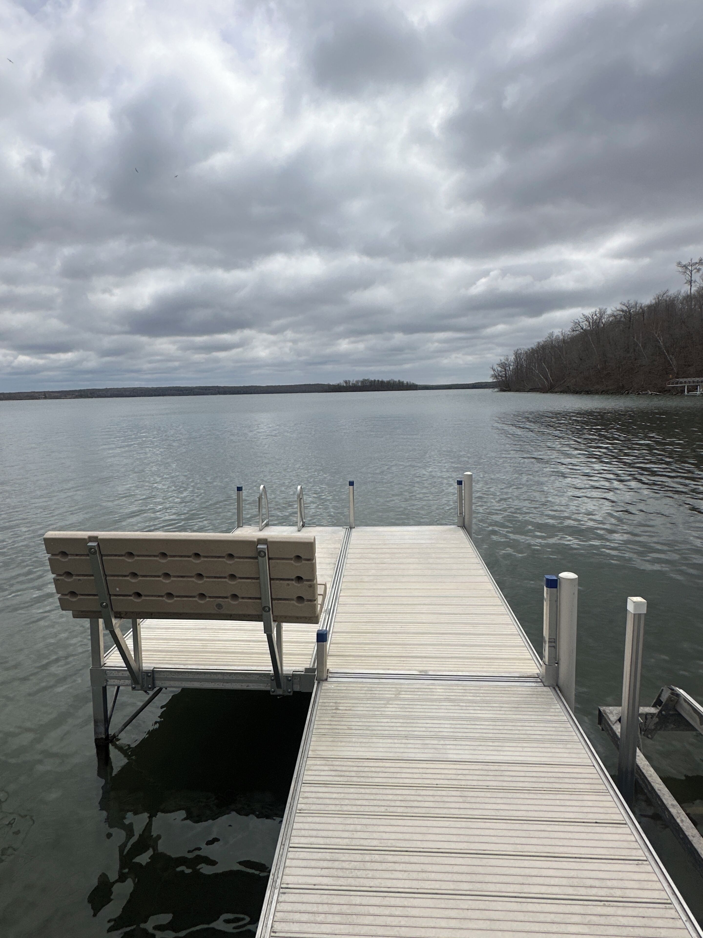 A wooden dock extending into a calm body of water with a bench at the end.