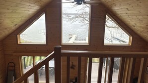 A wooden interior with a sloped ceiling, a ceiling fan, and a view of a dock through a large window. - Lakefront Escape with Loft & Summer Bunkhouse — Steps from the Water & Trails! (Waubun)