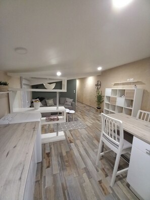 A modern, well-lit living room with a sofa, a dining table, and a bookshelf. - Gîte Adishatz (Sarrant)