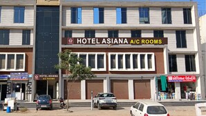 Un hotel llamado "Hotel Asiana A/C Rooms" con un letrero, varias ventanas y un árbol delante.