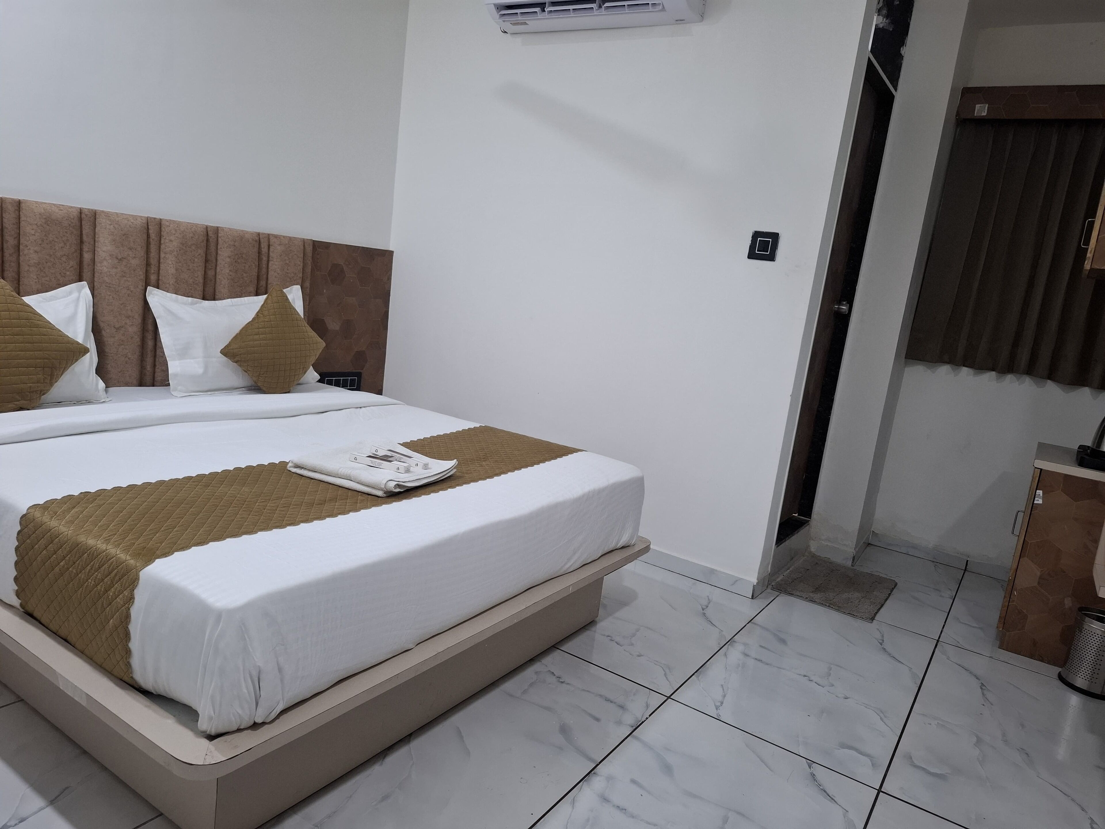 A neatly made bed with a brown throw blanket and pillows, a white headboard, and a small cabinet to the right.