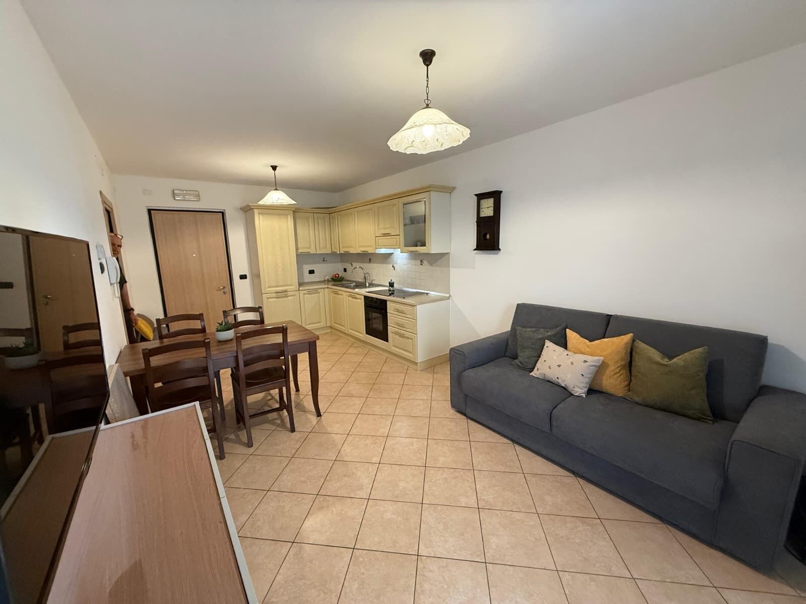 Un espace de vie compact comprenant un coin repas, une kitchenette et un canapé gris agrémenté de coussins.