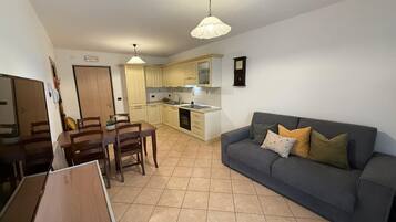 Een ruimtelijk ingerichte leefruimte met een eethoek, kitchenette en een grijze bank met kussens.