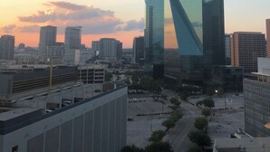 Un paysage urbain moderne, dominé par un imposant gratte-ciel en verre qui reflète les couleurs du coucher de soleil.