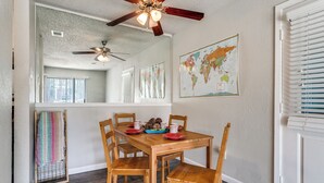 Un coin repas avec une table en bois, des chaises, un ventilateur de plafond et une carte du monde accrochée au mur.