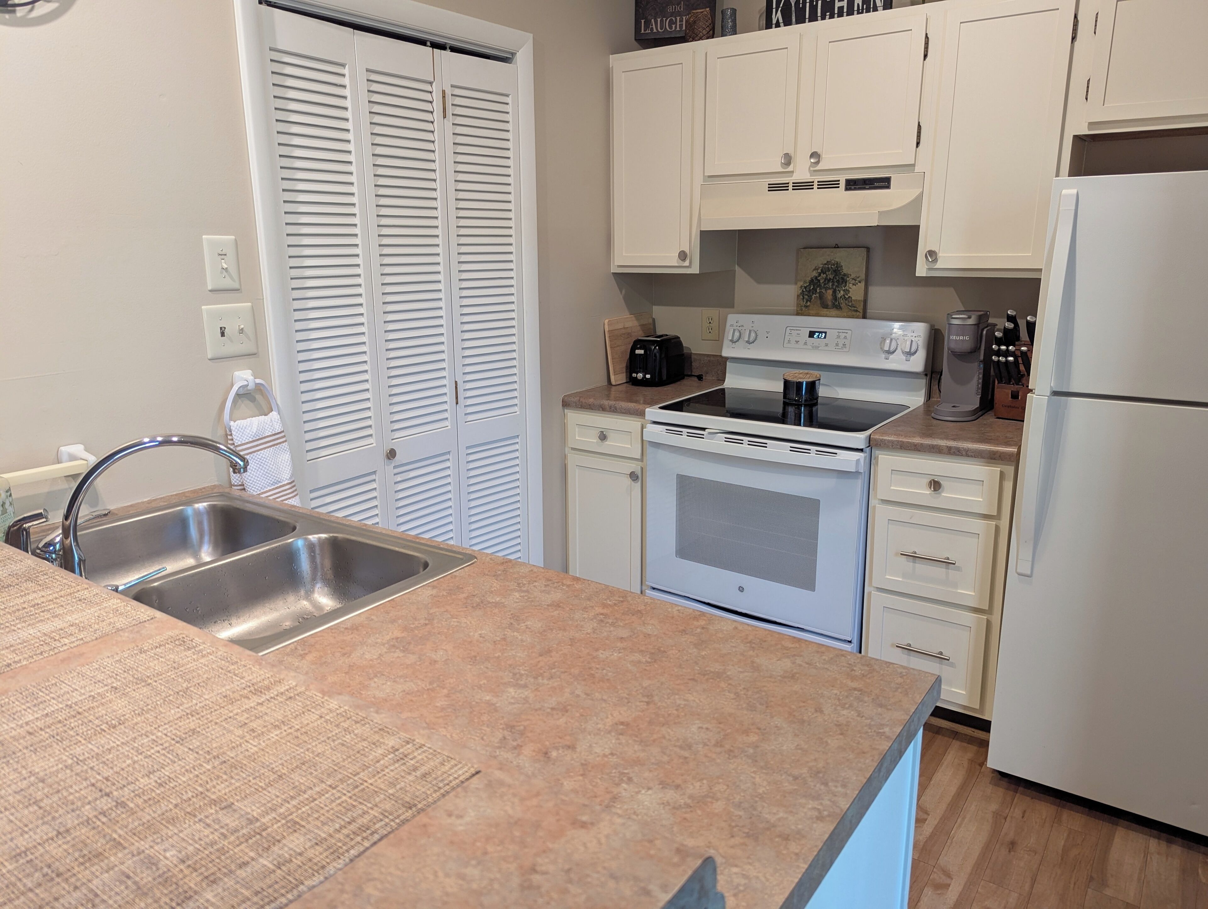 Una cocina con armarios blancos, un lavamanos de acero inoxidable, una estufa y un refrigerador.