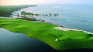 Un parcours de golf avec un plan d’eau, des bunkers de sable et quelques arbres.