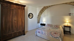 Un dormitorio con un amplio armario de madera, una cama con colcha estampada, un arco de piedra y dos lámparas de noche.