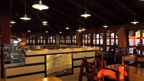 Un interno di ristorante con un'isola centrale, lampade a sospensione, tavoli e sedie in legno.
