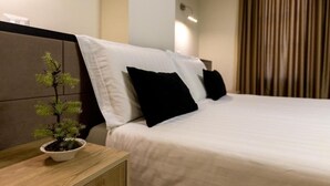 Un letto rifatto con cuscini bianchi e neri, una piccola pianta in vaso sul comodino e una testiera in legno.