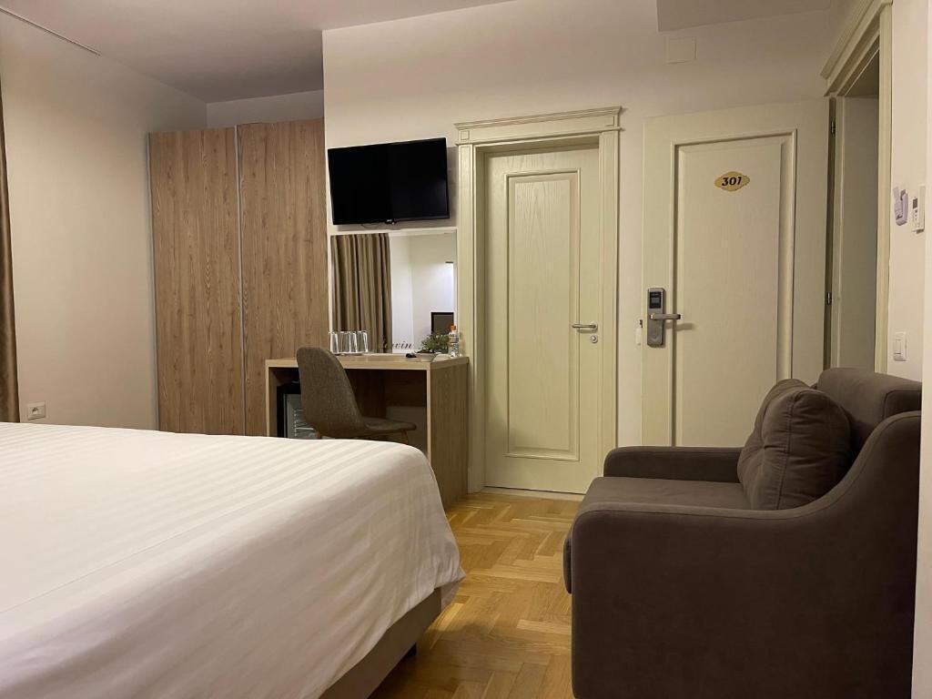 A hotel room with a bed, a desk, a TV, a door with a number, and a sofa.