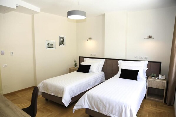 Habitación de hotel con dos camas individuales, piso de madera, una lámpara de techo y una mesita de noche con una planta.