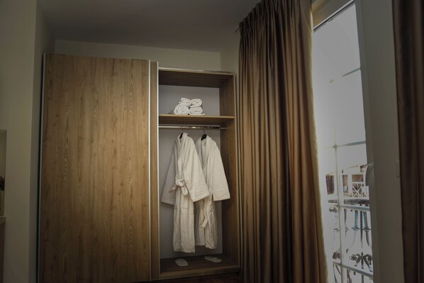 A wooden wardrobe with a mirror, a shelf with rolled towels, and two white bathrobes hanging.