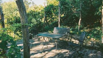Un espace extérieur aménagé dans un style rustique, avec une table et des bancs en bois, entouré de verdure et d’arbres.