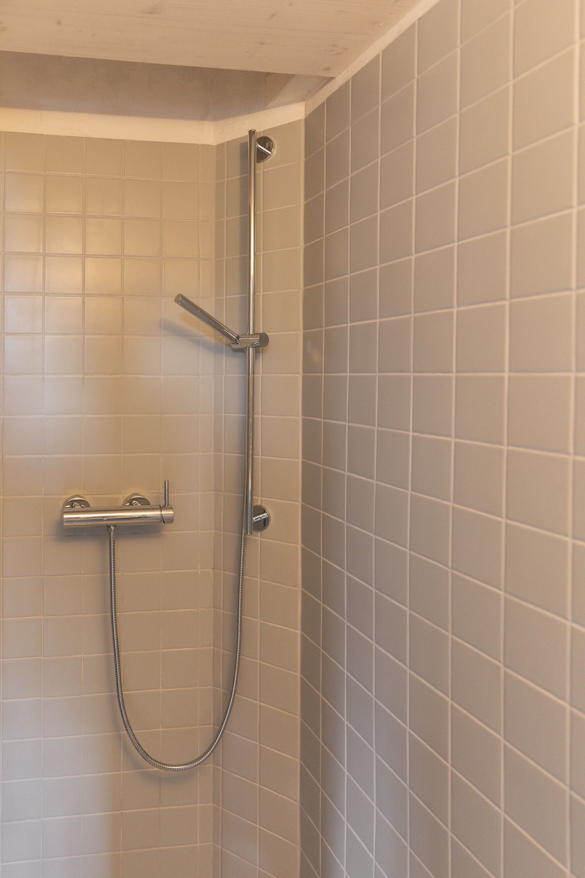 A shower with a handheld showerhead and a fixed showerhead, mounted on a tiled wall.