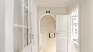 En hall med vita dörrar, en inramad tavla på väggen och en grön utrymningsskylt.