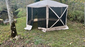 A Gazelle tent set up in a forested area with trees and grass around.