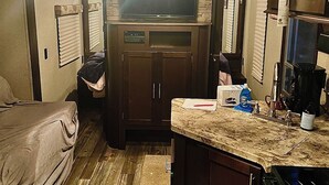 A compact RV kitchen with a built-in stove, a microwave, and a sink. There is a small seating area with a bench and a table.