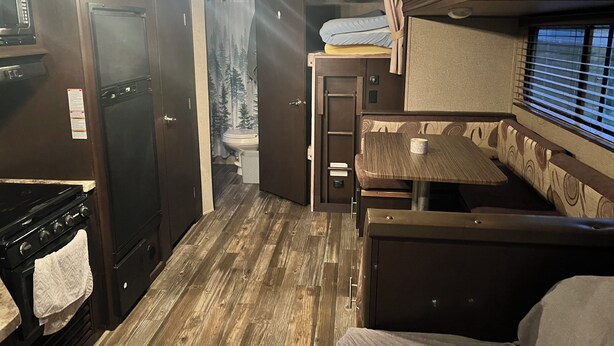 A compact RV interior with a kitchenette, a dining area, and a bathroom.