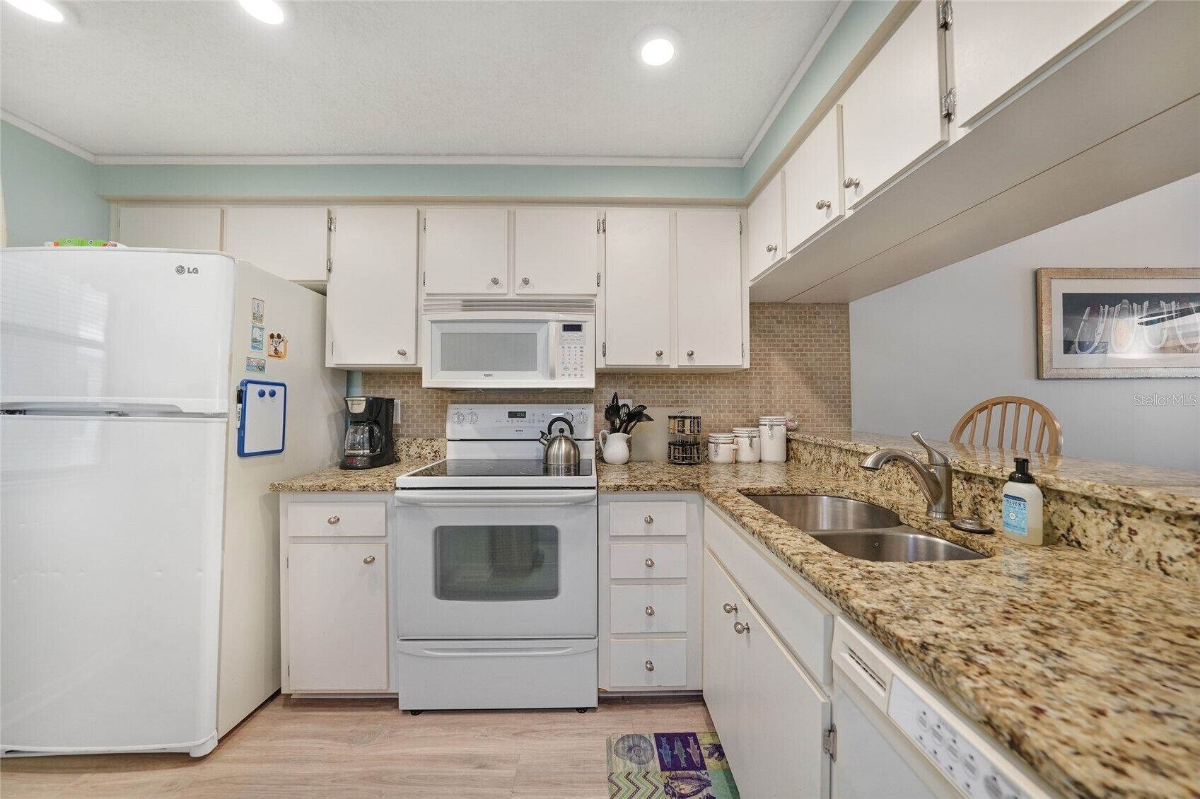 A kitchen with white cabinets, a microwave, a stove, a sink, and a refrigerator.