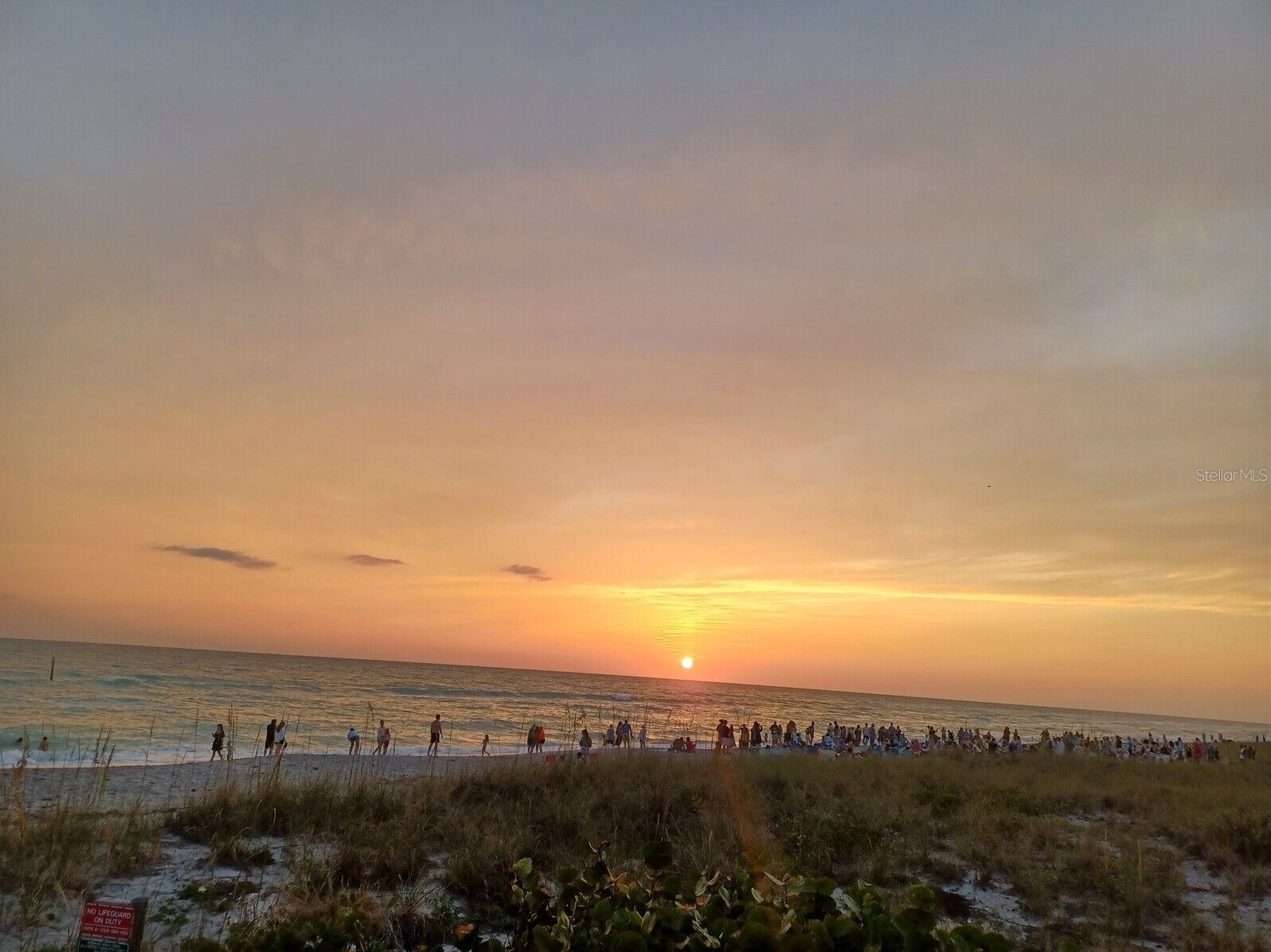 Una playa al atardecer, con gente caminando y sentada sobre la arena.