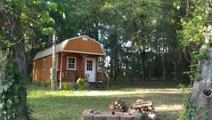 A small cabin with a porch, surrounded by trees and a pile of firewood in front. - Peacefull Cabin in the Woods with heat/air conditioning (Marietta)