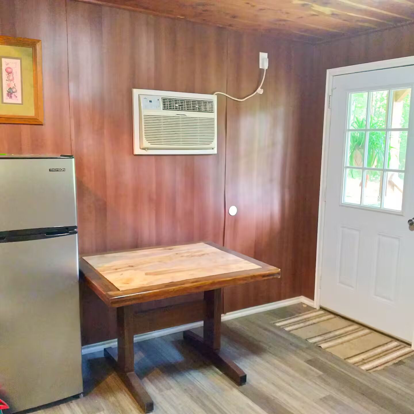 Eine Küche mit Kühlschrank, einem Holztisch und einer Wand-Klimaanlage.