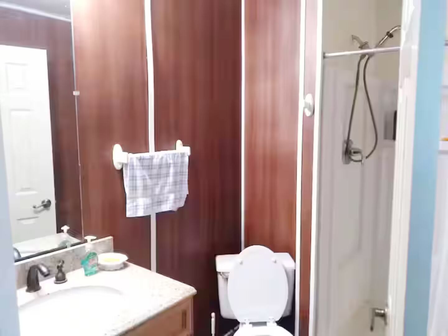 Une salle de bain avec un meuble-lavabo en bois, un lavabo blanc, des toilettes et un espace douche.