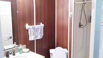Une salle de bain avec un meuble-lavabo en bois, un lavabo blanc, des toilettes et un espace douche.