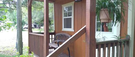 A wooden porch with a bench, a potted plant, and a window.