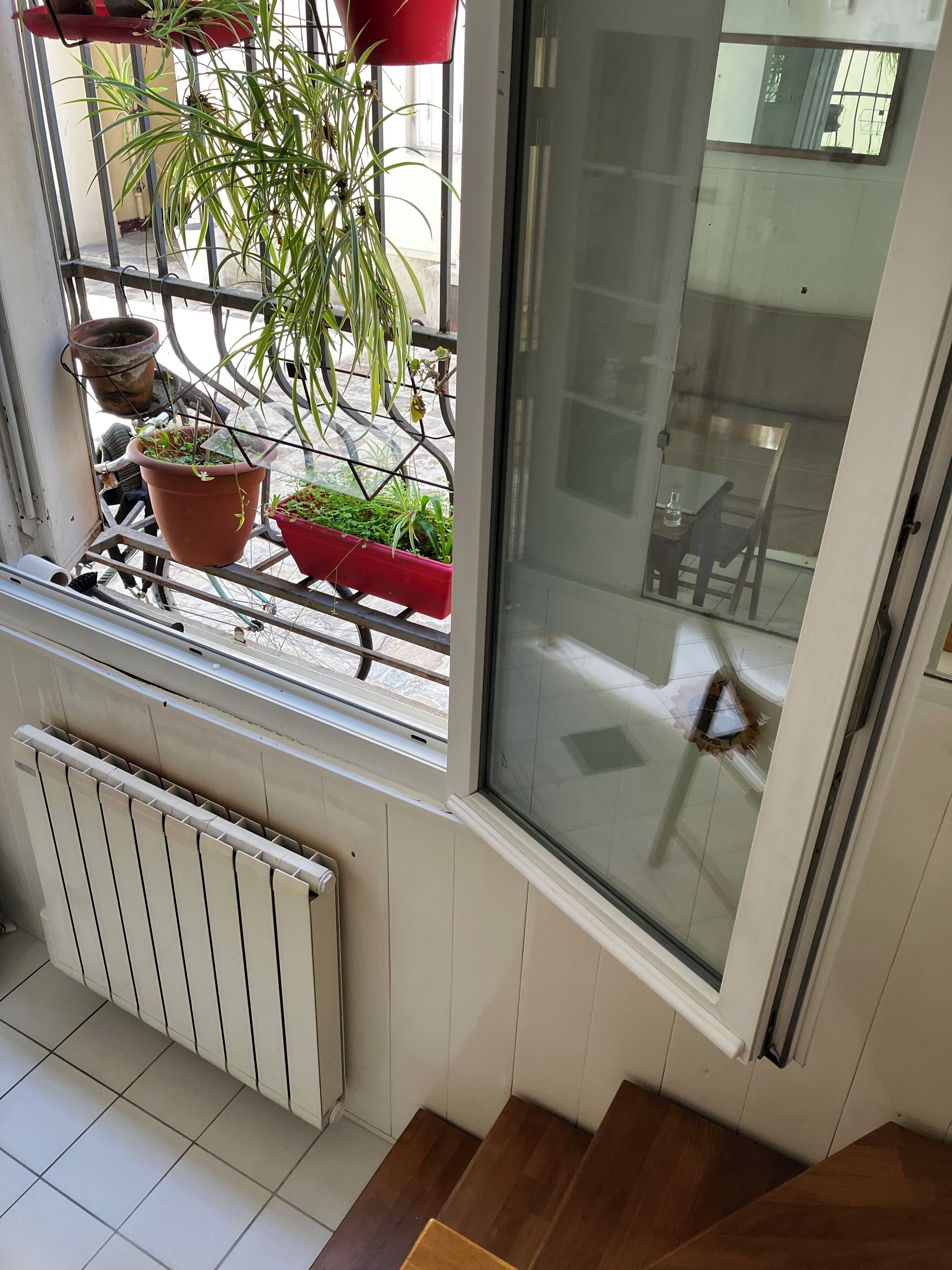 Une pièce avec une fenêtre donnant sur un balcon, un radiateur et un escalier en bois.