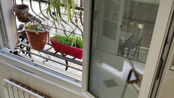 Une pièce avec une fenêtre donnant sur un balcon, un radiateur et un escalier en bois.
