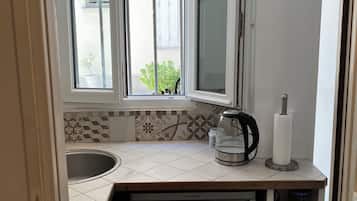 A compact kitchen with a built-in dishwasher, a window with decorative iron bars, and a small sink.