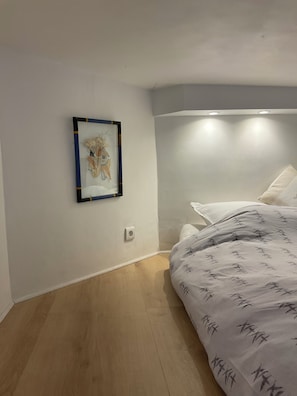 A bedroom with a bed, a wall-mounted picture, and a light fixture.