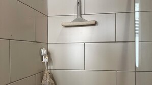 A shower area with a handheld showerhead mounted on the wall, a towel rack with a towel, and a shower control knob. - Charming apartment Paris center république (Paris)